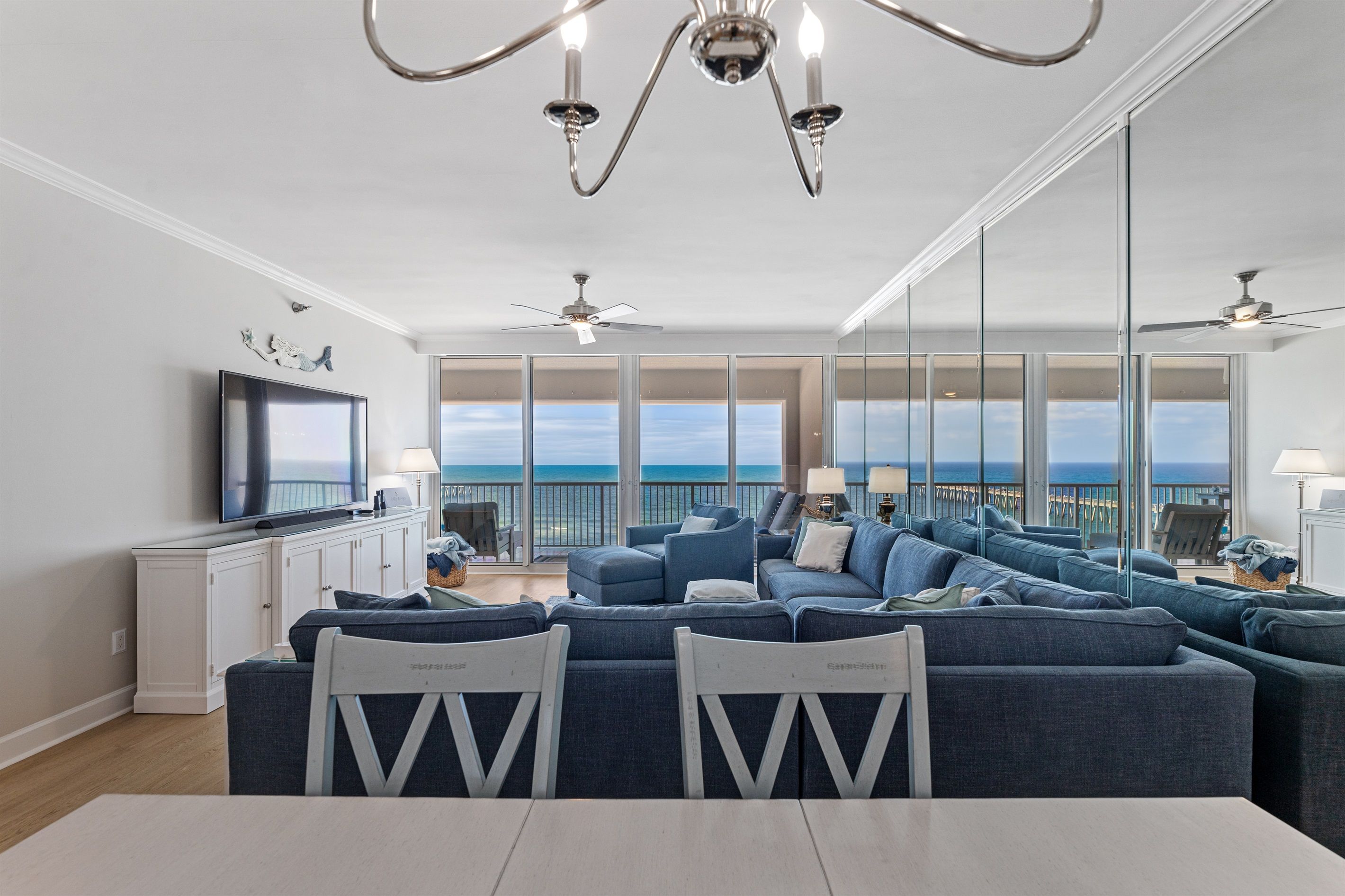 Un salon spacieux avec un grand canapé d’angle, un téléviseur à écran plat et un balcon offrant une vue sur l’océan.