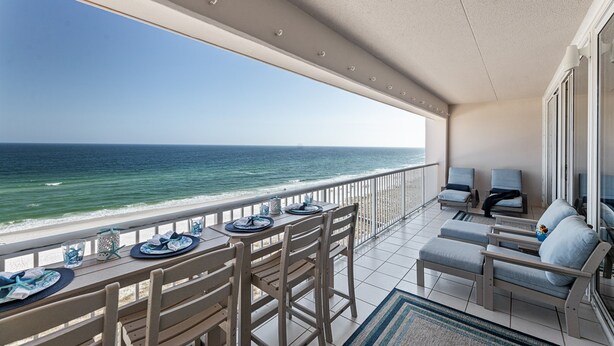 A balcony with a view of the ocean, a dining table set with plates and glasses, and two sofas. - Salty Breezes (Navarre)