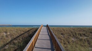 A wooden boardwalk leading to a beach with a pier in the distance. - Salty Breezes (Navarre)