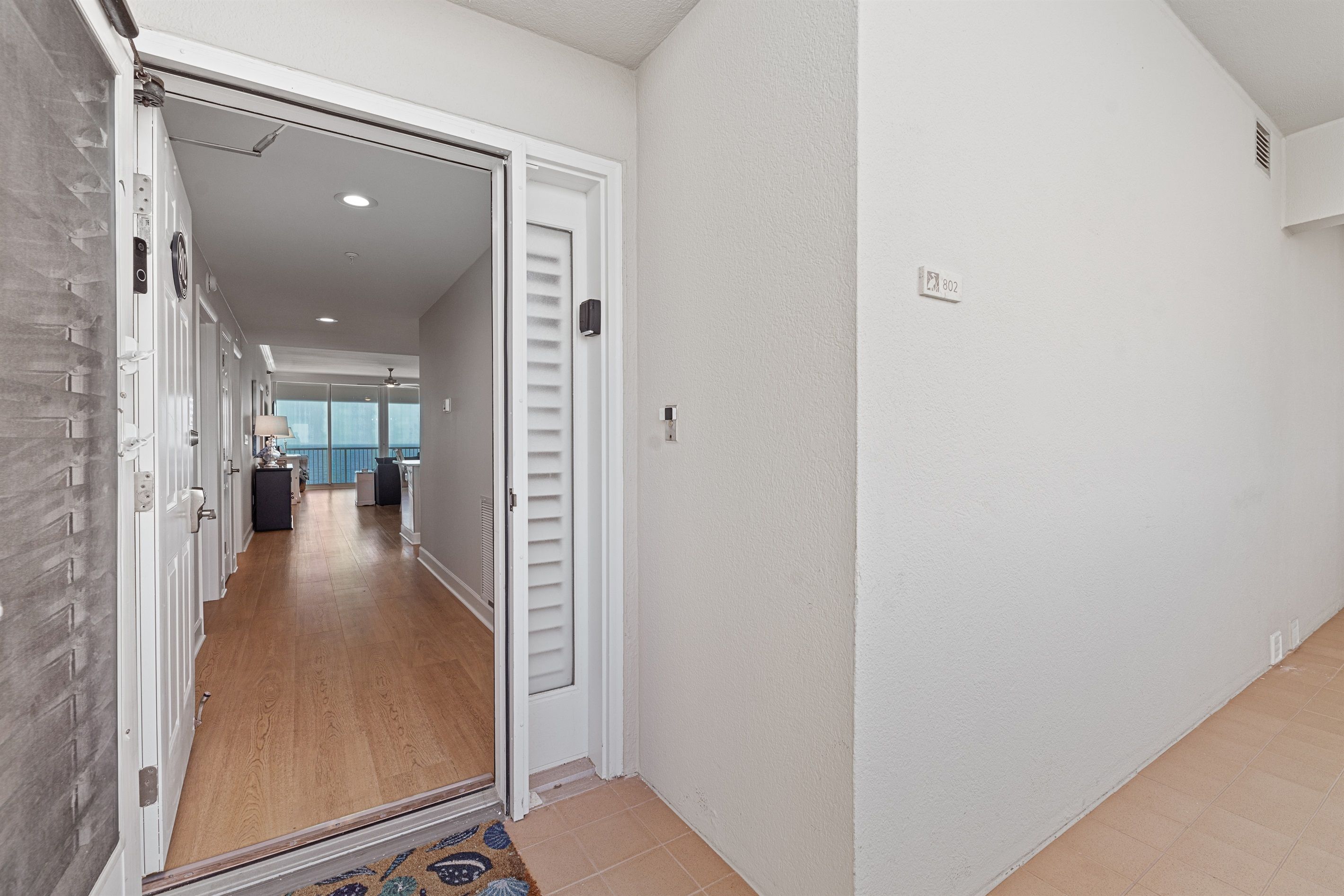 Un couloir doté d’un plancher en bois, de murs blancs et d’une porte donnant sur une pièce avec vue.
