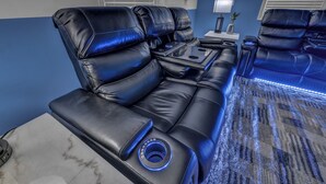 A black leather sofa with a massage function, a small table with a lamp, and a patterned rug.
