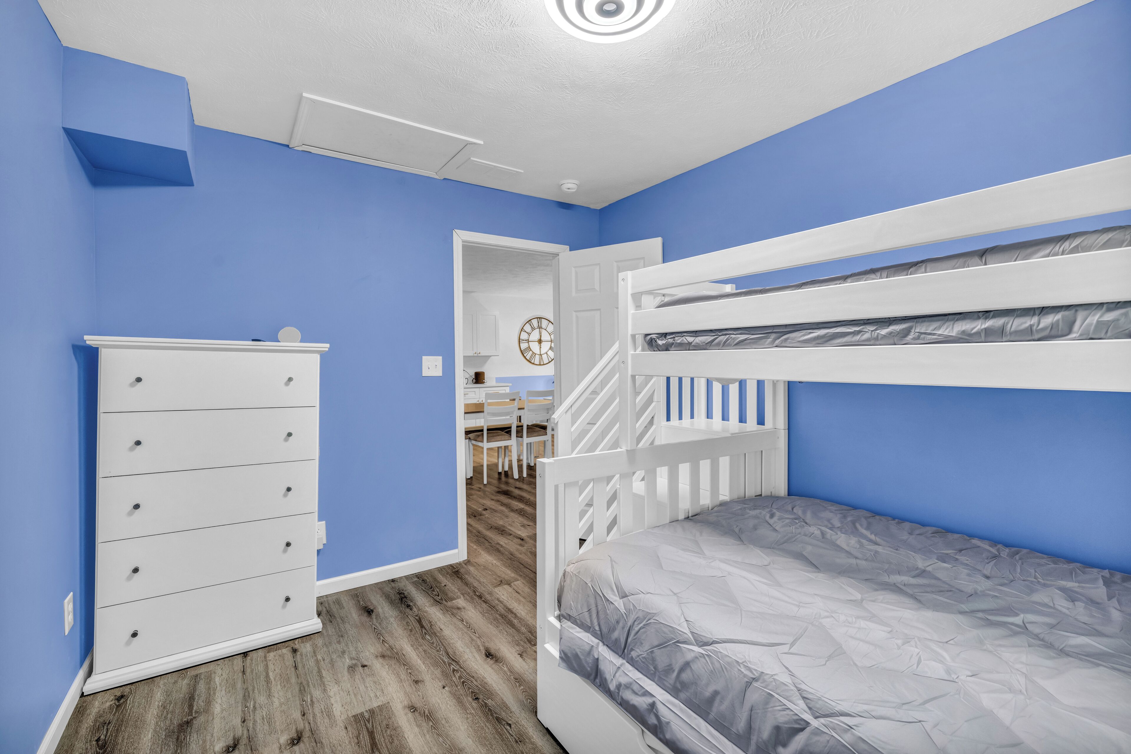 A bedroom with blue walls, a white dresser, a bunk bed, and a wooden floor.