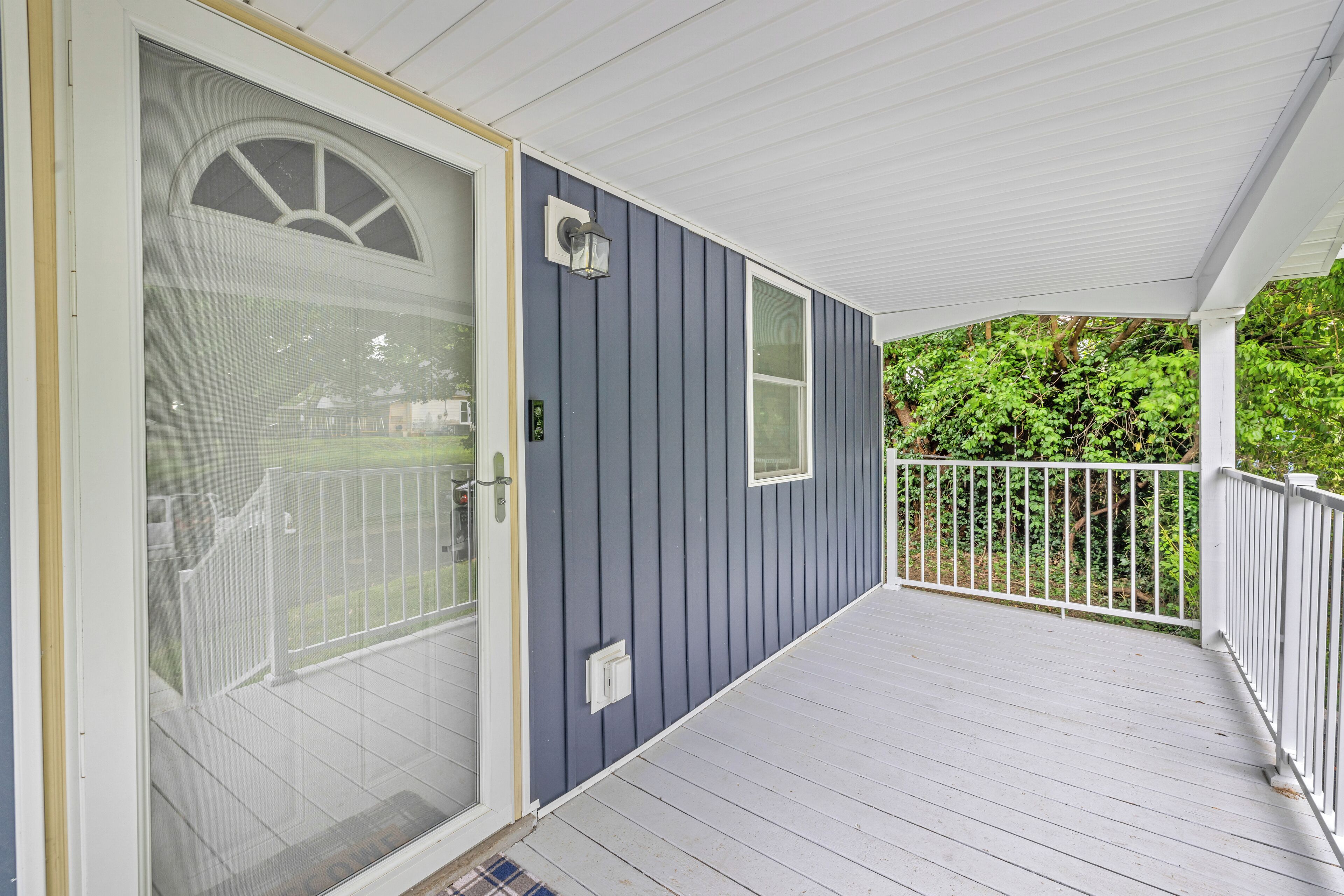 A covered porch with a white railing, a glass door with a white frame, and a blue exterior wall.