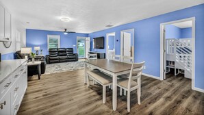 A modern living room with a dining area, blue walls, wooden flooring, and a staircase.