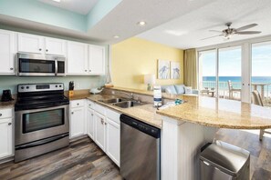 A kitchen with a microwave, oven, and dishwasher, a large island with a sink, and a view of the ocean. - Waters Edge 308 • Amazing Beach Condo with Oceanfront Balcony, Covered Parking, Free Beach Service (Fort Walton Beach)