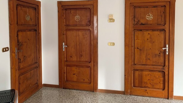 Une pièce dotée de deux portes en bois, chacune munie d’une poignée et d’une serrure. Un interrupteur et un thermostat sont fixés au mur, entre les deux portes.