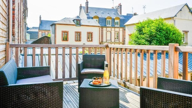 Un balcon agrémenté de meubles en osier, une table avec des boissons et des en-cas, et une vue sur les bâtiments en arrière-plan.
