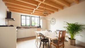 A modern kitchen with wooden beams, a dining table with chairs, a potted plant, and a window with a view.