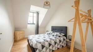 A bedroom with a sloped ceiling, a bed with a geometric-patterned bedspread, a bedside table with a lamp, and a wooden ladder leaning against the wall.