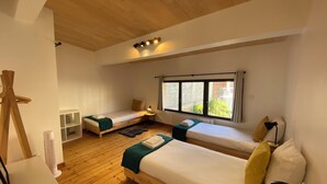 A room with two wooden beds, a standing fan, and a window with curtains.
