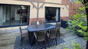 A modern house with a patio area featuring a table and chairs, large windows, and a brick wall.