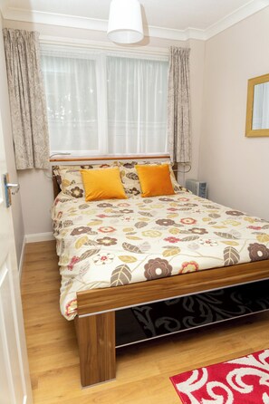 A bedroom with a bed, curtains, a window, a radiator, and a wooden floor.