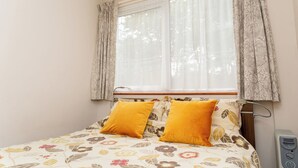 Un dormitorio con colcha estampada, dos almohadas amarillas, una ventana con cortinas translúcidas y un calentador de pared.