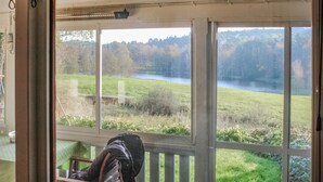 Ein Zimmer mit großen Fenstern, die auf ein grünes Feld und einen See blicken.