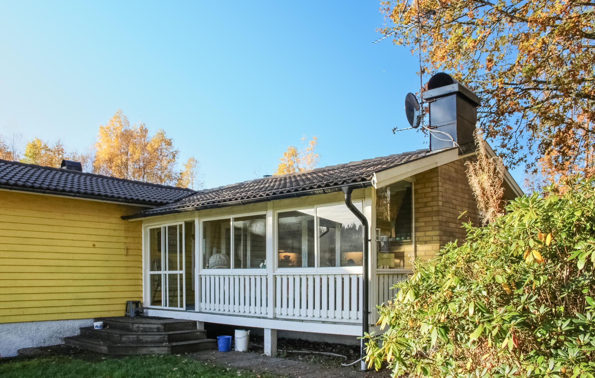 Une maison jaune avec un porche et une antenne parabolique.