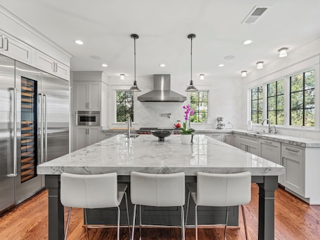 A modern kitchen with a large island, stainless steel appliances, and pendant lighting.