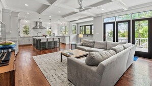 A modern kitchen with a central island, a dining area with a grey sofa, and large windows offering a view of the outdoors. - Glebe Getaway House (Arlington)