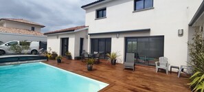 Une maison moderne dotée d’une piscine, d’un espace salon extérieur et de plantes en pot.
