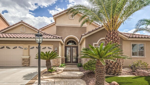 A residential house with a stone facade, a front entrance with a glass door, and a driveway leading to a garage. - Tranquil Henderson Retreat with Pool & Spa! (Henderson)