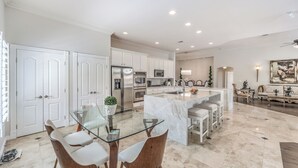 A modern kitchen with white cabinetry, stainless steel appliances, and a glass dining table. - Tranquil Henderson Retreat with Pool & Spa! (Henderson)