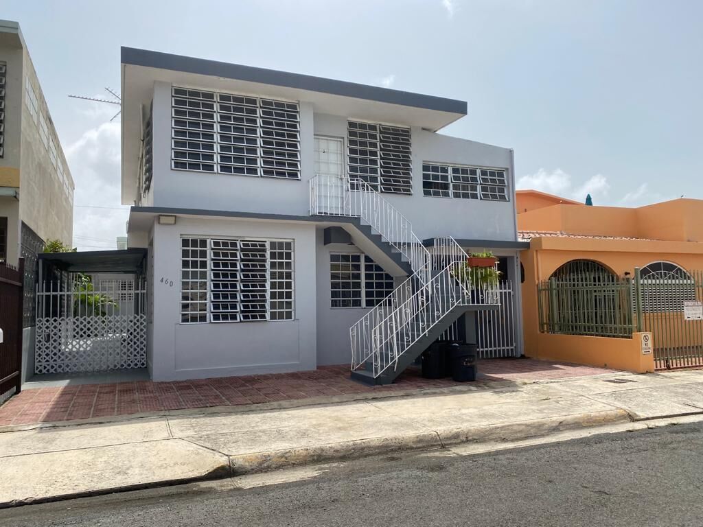 A two-story building with a white facade, a central staircase, and a gated entrance.