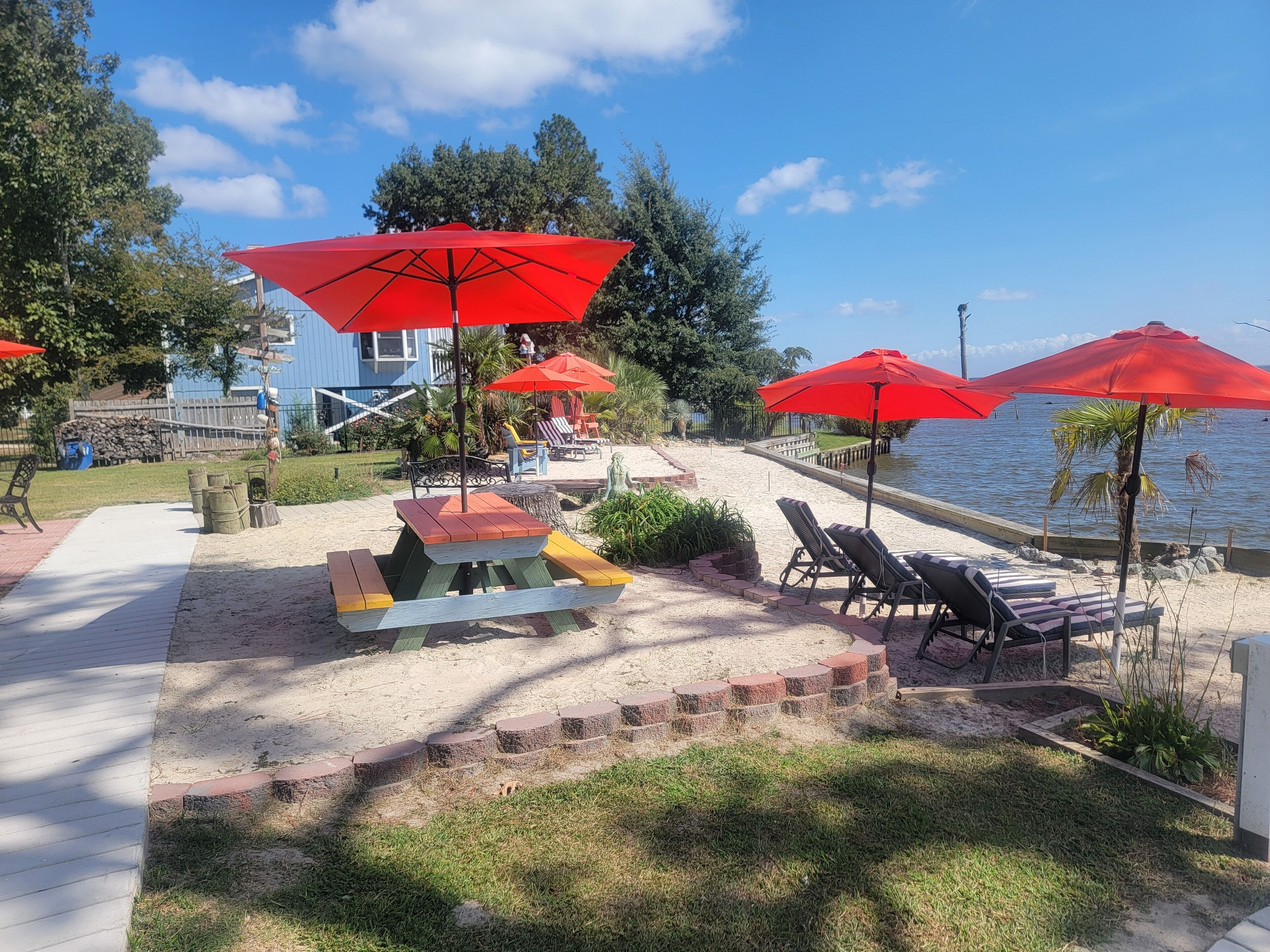 Une terrasse au bord de la plage, agrémentée de parasols rouges, de chaises longues et d’une table de pique-nique.