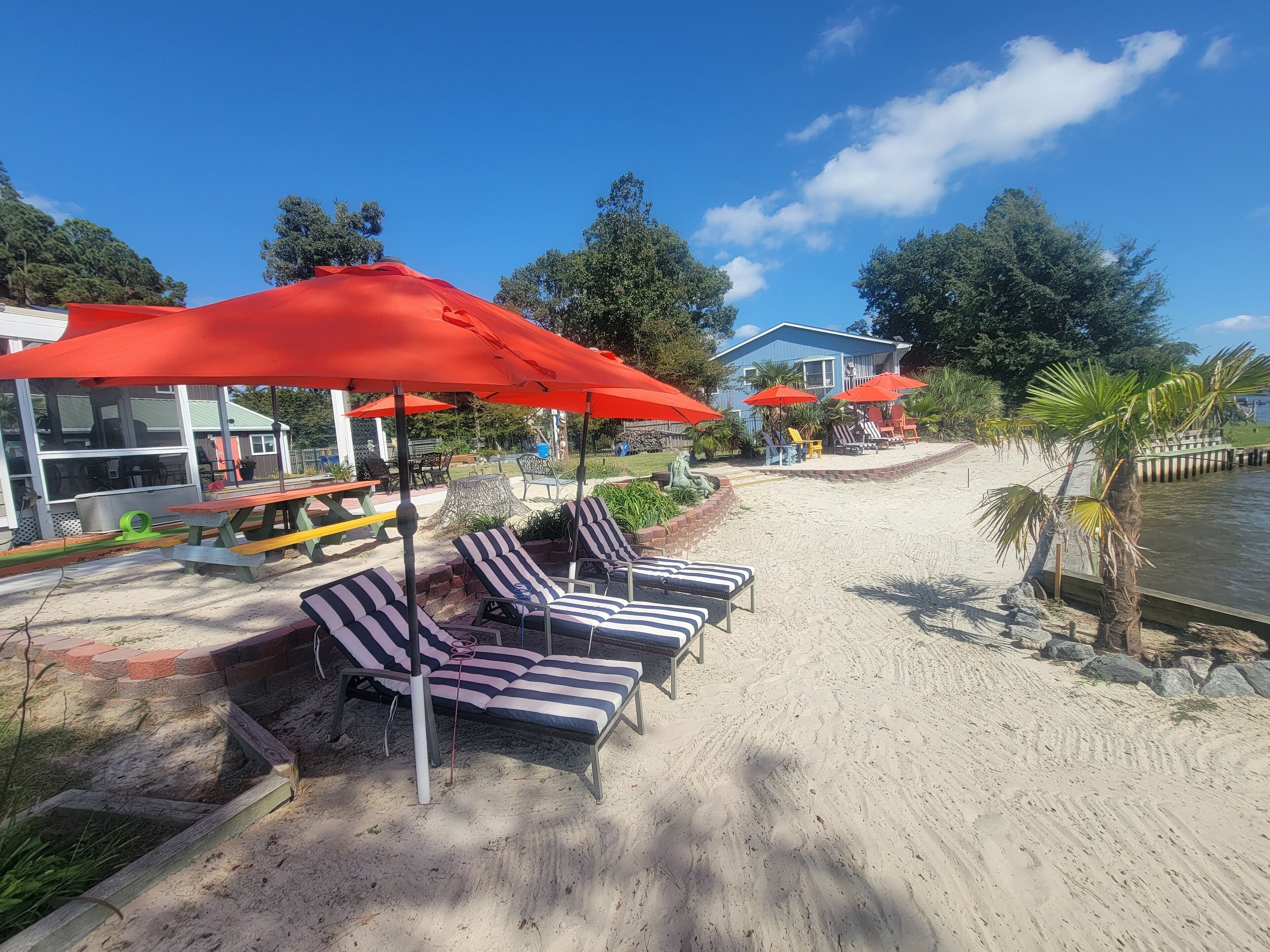 A beachside area with lounge chairs and red umbrellas, a sandy beach, and a house in the background.