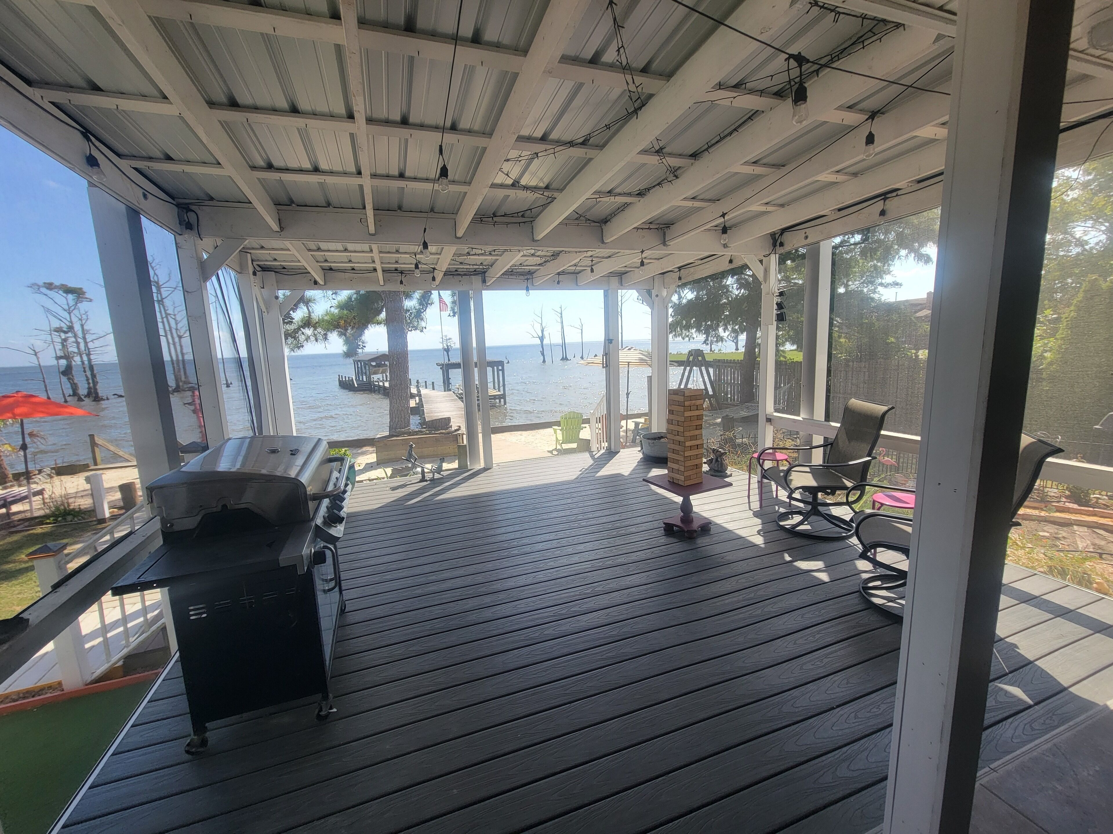 Eine überdachte Terrasse im Freien mit Grill, Sitzgelegenheiten und Blick auf das Wasser.