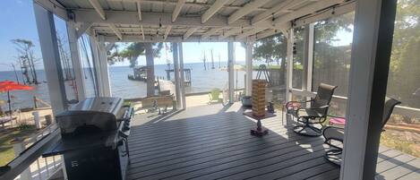 Eine überdachte Terrasse im Freien mit Grill, Sitzgelegenheiten und Blick auf das Wasser.