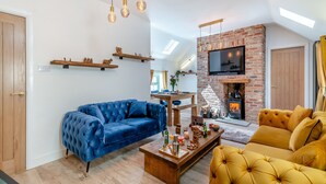 Ein modernes Wohnzimmer mit einem blauen Sofa, einem gelben Sofa und einem Holztisch. Ein Kamin aus Ziegelsteinen ist vorhanden, darüber ist ein Fernseher angebracht.