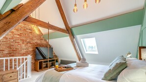Ein gemütliches Schlafzimmer unter dem Dach mit freiliegenden Holzbalken, einer Backsteinwand, einem erhöhten Fernseher und einem kleinen Fenster.