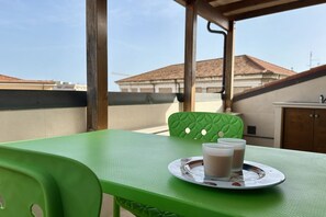 A green table with a tray holding two glasses of a beverage, a green chair, and a view of buildings in the background.