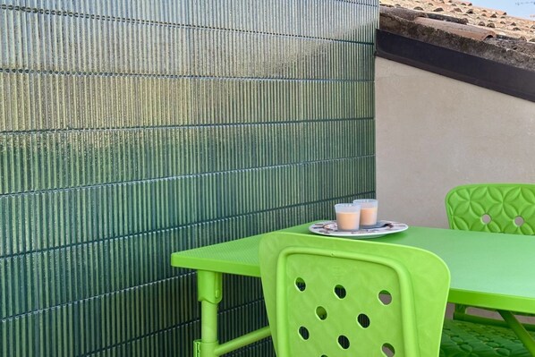 Una pared metálica verde con textura corrugada, una mesa verde con una bandeja de bebidas y una silla verde.