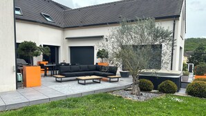 A modern outdoor patio with a black sectional sofa, wooden coffee table, and orange accent pieces.