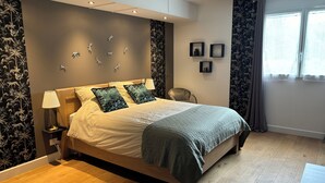 A modern bedroom with a bed, a nightstand, a chair, and a window.