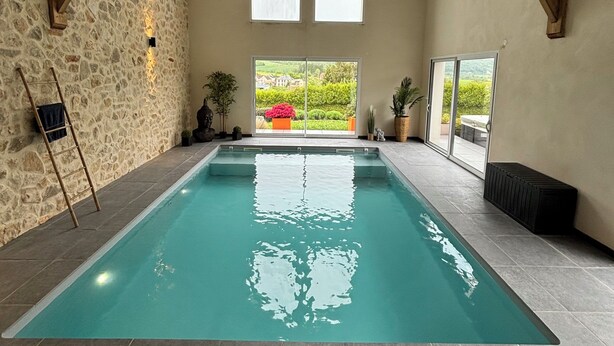 An indoor swimming pool with stone walls, wooden beams, and a view of greenery outside.
