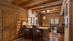 A log cabin kitchen with wooden walls, a central island with bar stools, a stove, and a microwave. - Great Condo close to the mountain (Breckenridge)