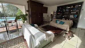 Un salon comprenant un canapé, une table basse et une bibliothèque. Une grande fenêtre offre une vue sur une piscine.