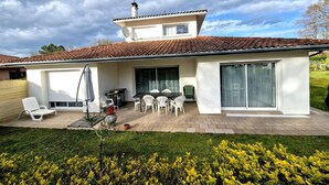 A two-story house with a tiled roof, a patio with outdoor furniture, and a large sliding glass door. - Villa Dunisia - Leon (LEON)