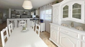 A spacious dining area with a white table and chairs, a decorative vase, and a white cabinet with glass doors. - Villa Dunisia - Leon (LEON)
