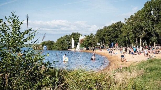 A beach with people swimming and walking, a sailboat, and a sandy shore with trees. - Villa Dunisia - Leon (LEON)