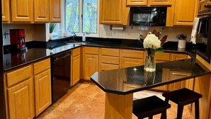 Una cocina con armarios de madera, encimera negra, microondas de acero inoxidable y un florero con flores en la isla.