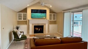 Una sala de estar con chimenea, un televisor montado encima y un sillón verde, además de un gran ventanal con vistas al exterior.