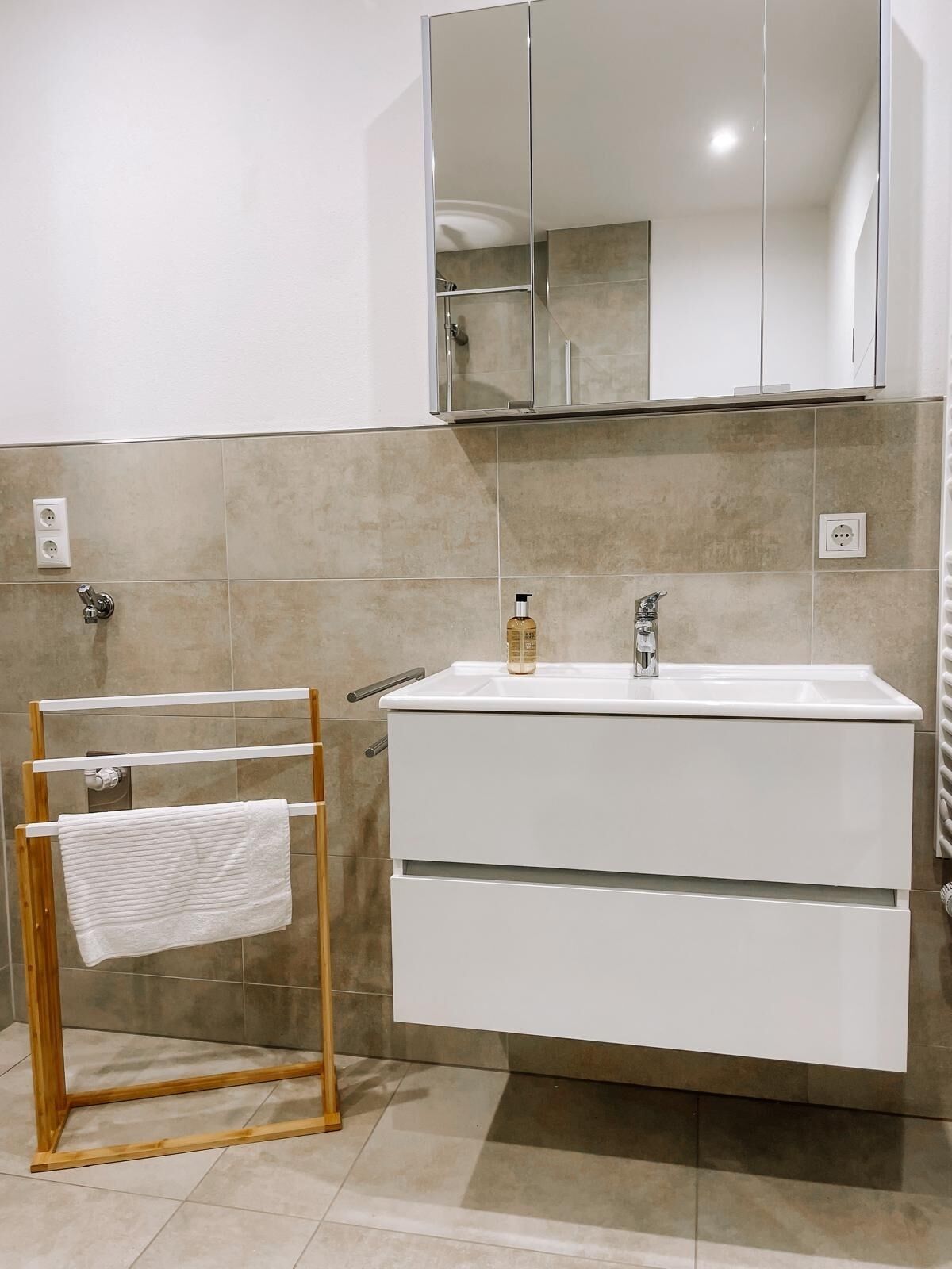 Une salle de bain moderne avec un meuble-lavabo blanc, un miroir au-dessus du lavabo et un porte-serviettes sur lequel est posée une serviette blanche.