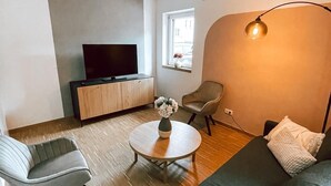 Un salon moderne avec un canapé, une table basse ronde et un téléviseur posé sur un meuble en bois.