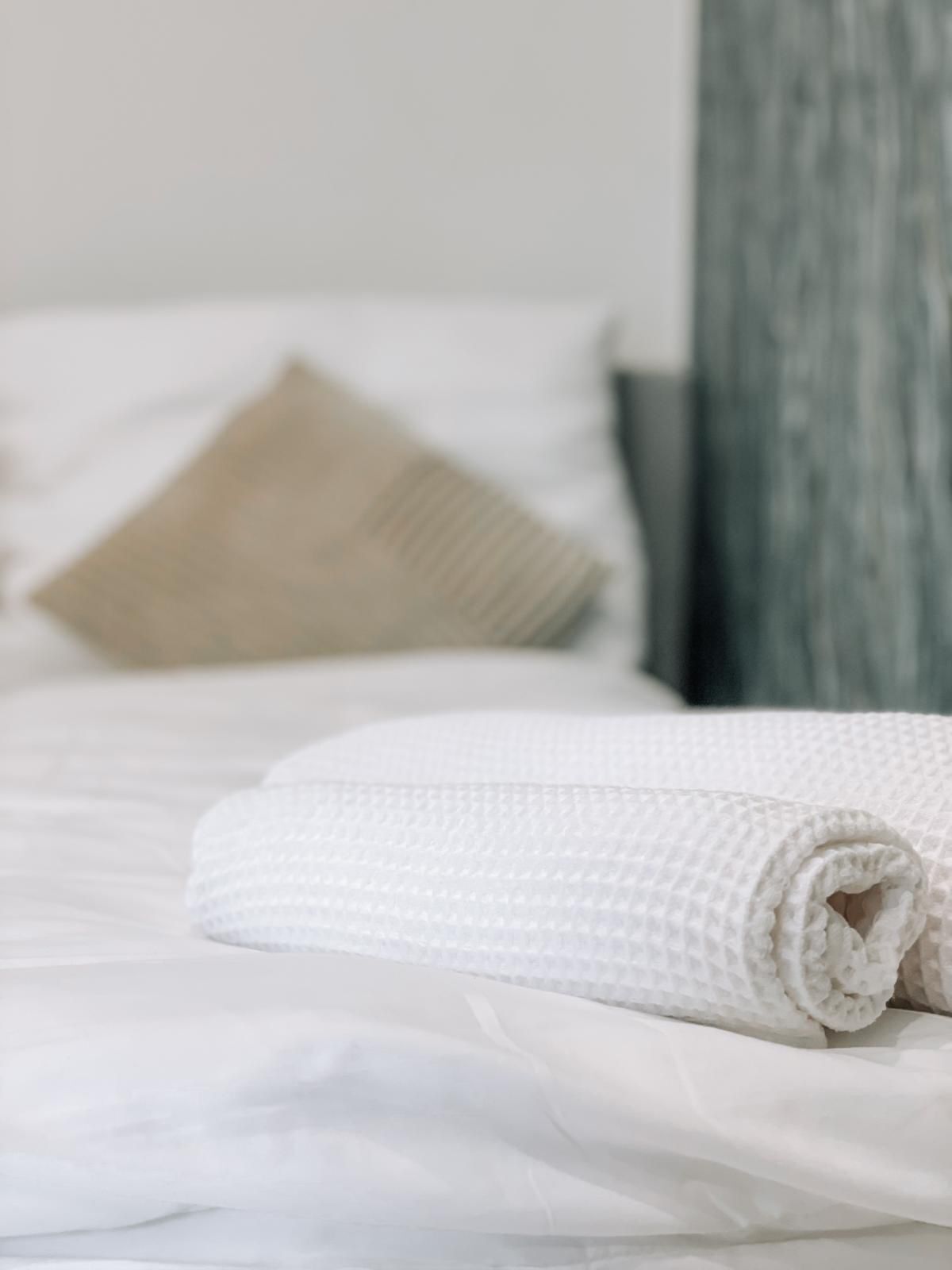 Una cama bien hecha con sábanas blancas y una toalla enrollada.