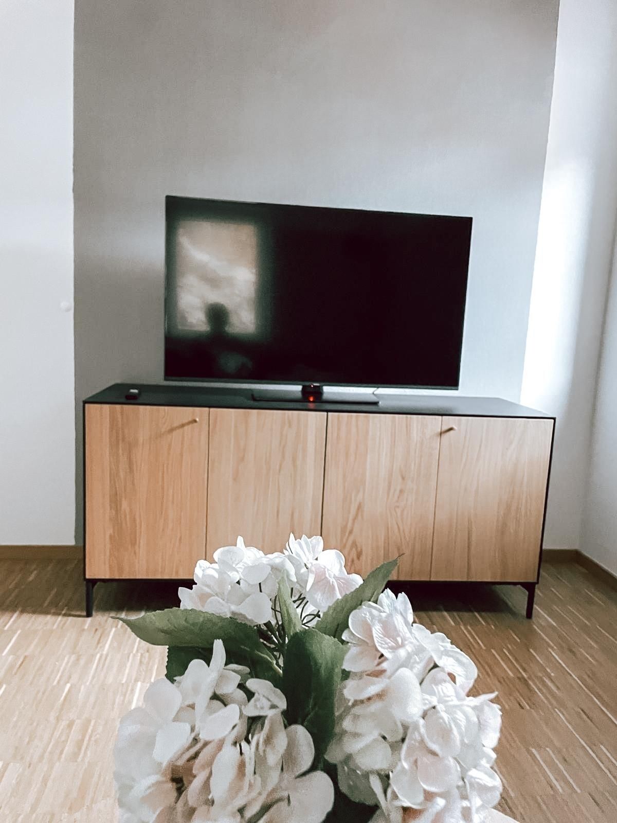 A flat-screen TV on a wooden cabinet with a floral arrangement in front.