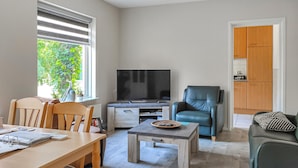 A living room with a TV, a dining table, chairs, a coffee table, a sofa, and a kitchen area with wooden cabinets. - Nice home in Kilder with kitchen (Kilder)