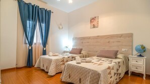 Une chambre avec deux lits, une tête de lit en bois, un globe terrestre posé sur une table de chevet et une fenêtre avec des rideaux bleus.