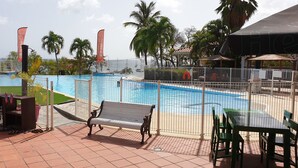 Un espace piscine doté d’une terrasse entourée d’une clôture, de bancs et d’une table avec des chaises.